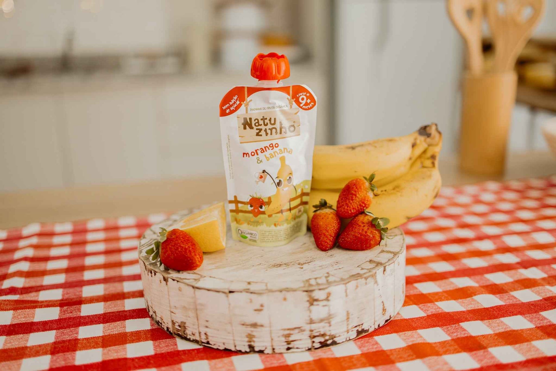 Papinha Organica Natural de Fruta sabor Morango e Banana Natuzinho - embalagem em cima de balcao, com pedaço de fruta - banana e morango - ao lado