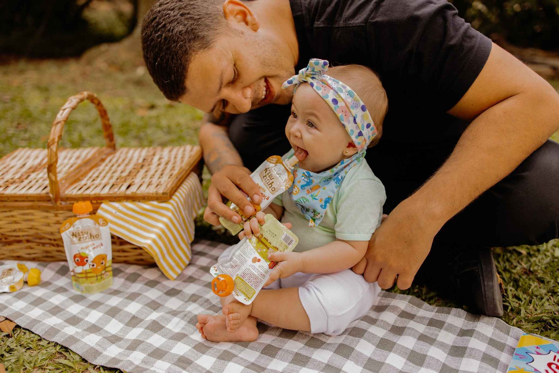 Papinha Organica Natural de Fruta sabor Manga e maça Natuzinho - pai alimentando a bebe no parque com natuzinho sabor manga e maça