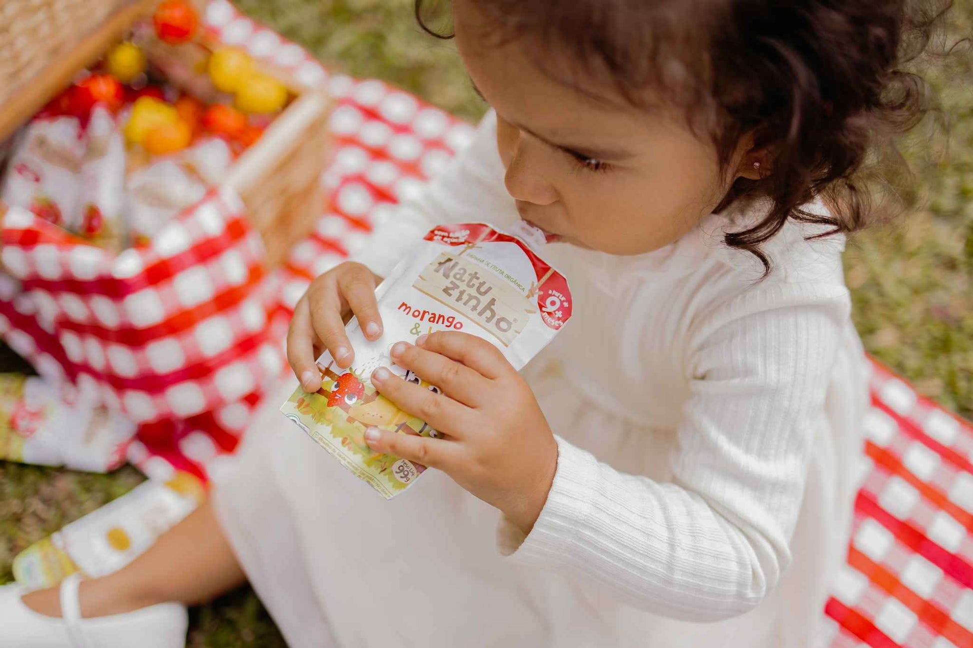 Papinha Organica Natural de Fruta sabor Morango e Banana Natuzinho - criança sentada no parque, comendo papinha